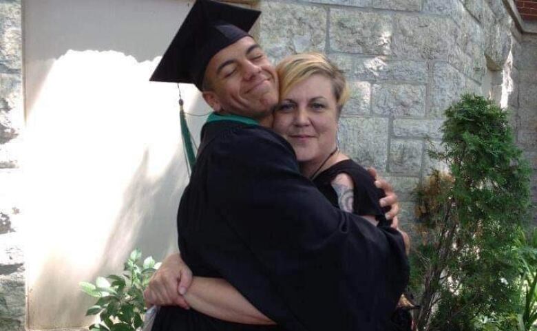 A man in a cap and gown hugs a woman with blonde hair.