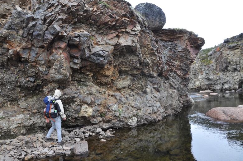 A group of people walk along the rocky edge of water.