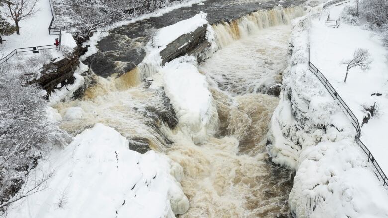 Water flows quickly down a river with the river banks covered in snow.