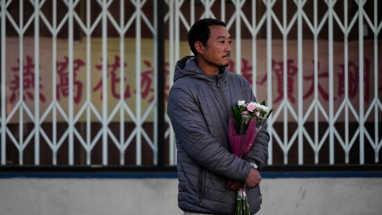 A man stands alone holding a bouquet of flowers, looking sad. 