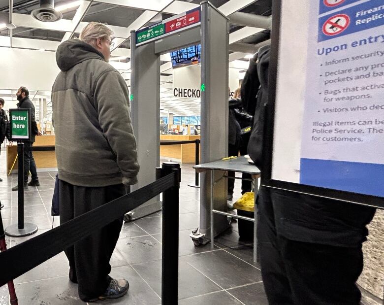 A person in a grey hooded jacket waits to go through a metal detector.