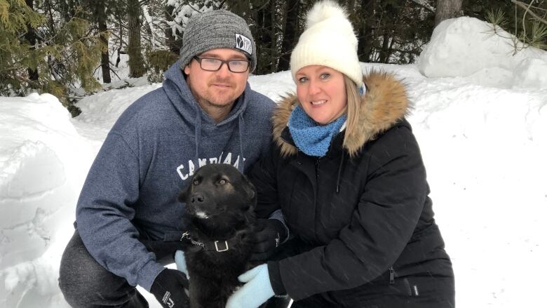 A man and woman kneeling behind a black dog.