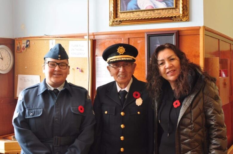 A group of three people smile at the camera at a Remembrance Day cermoney in Eskasoni. 