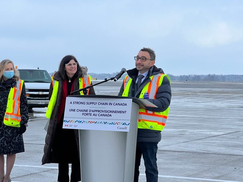 A man speaking at a podium and a woman standing beside him and looking at him.