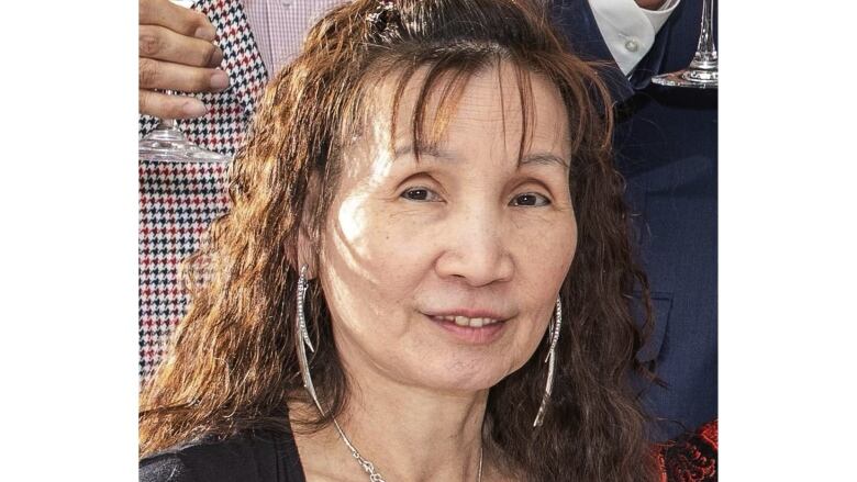 A woman with shoulder-lenth brown curly hair, wearing long silver earrings. 