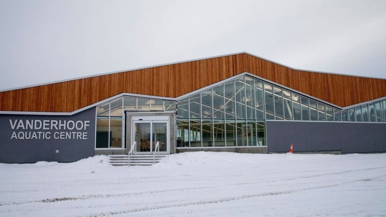 A long low wood frame building with a glass front that says Vanderhoof Aquatic Centre. The ground is covered in snow.