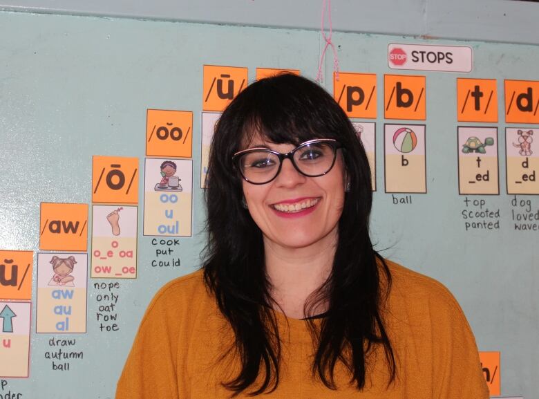 close up young woman with glasses and dark hair in front of a board with vowels and illustrations