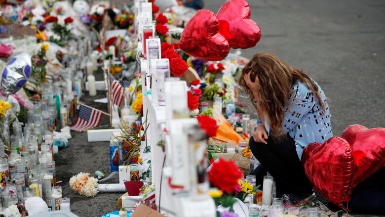 A woman places a palm on her head while kneeling before crosses, candles and flowers.