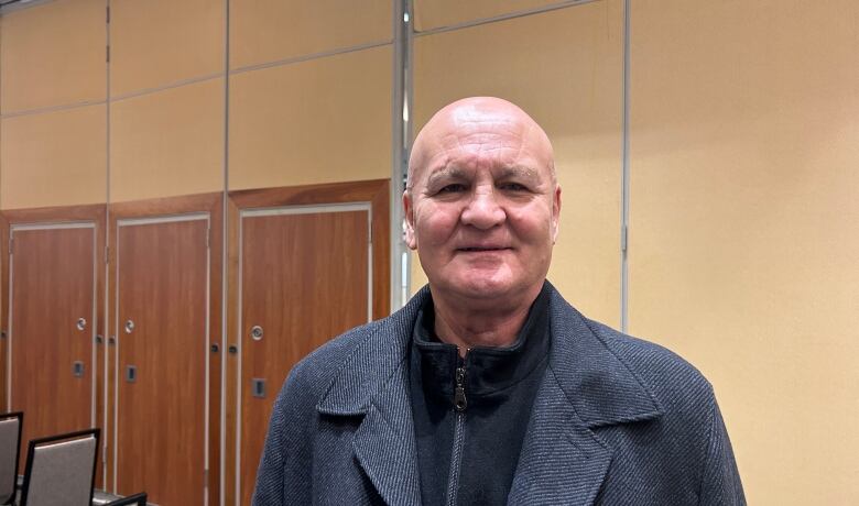 A bald man poses for a photograph in a room lined with chairs.