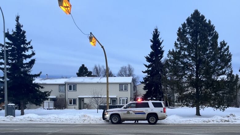 An RCMP vehicle sits parked at the side of a snowy road in a residential neighbourhood.