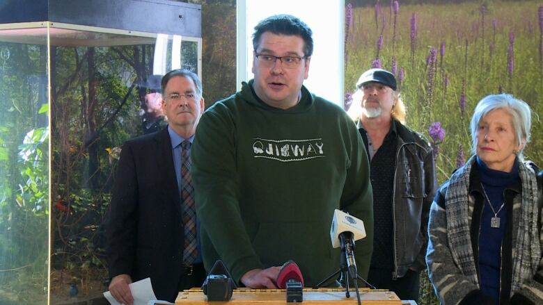 A man wearing a green hoodie standing at a podium delivering a speech to reporters