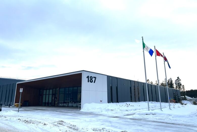 A rectangular building is seen on a winter's day with three flag poles out front.