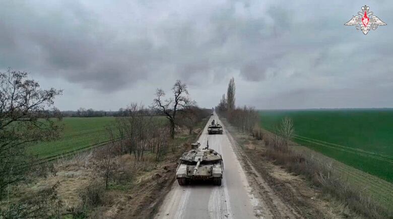 Two tanks are shown travelling down a rural road, green fields on either side.