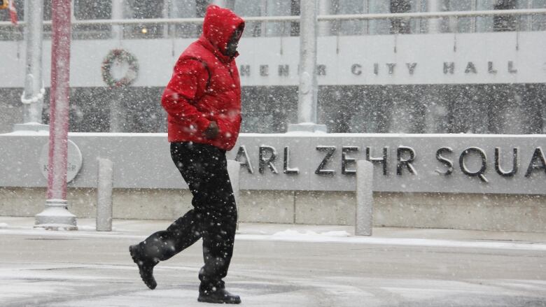 Man in red coat walks through snow flurries