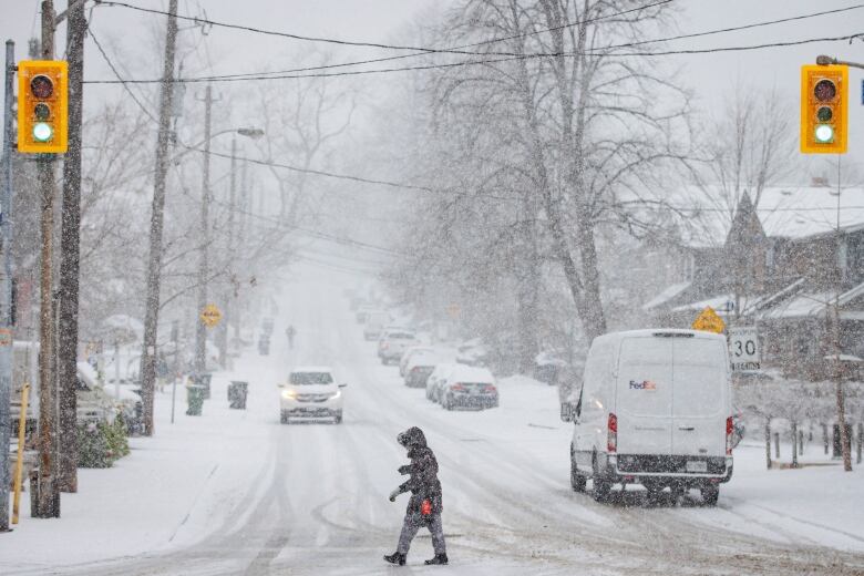 A pedestrian crosses a street at the start of a significant snowstorm in uptown Toronto on Jan. 25, 2023.