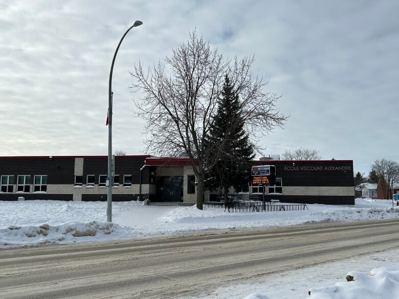 A brown school is pictured from across a residential street and it's surrounded by snow