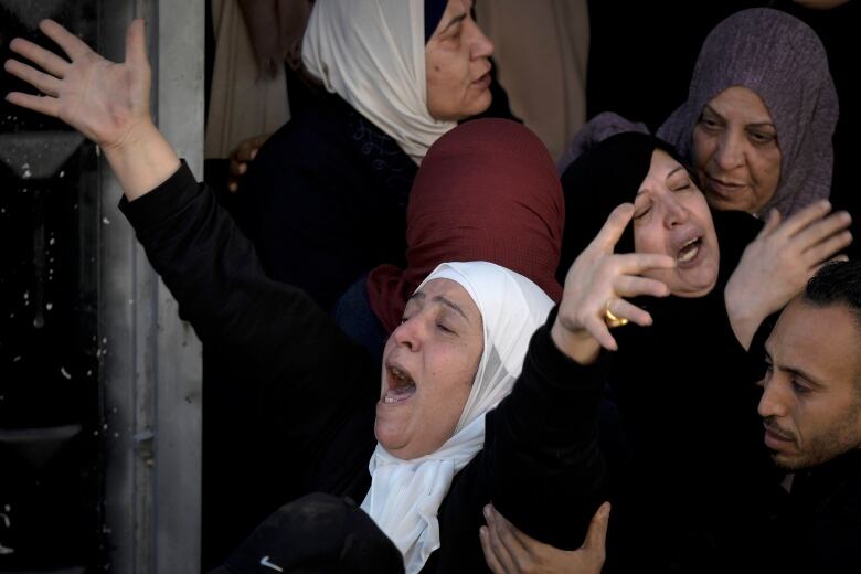 Several women in headscarves are shown gesturing. 