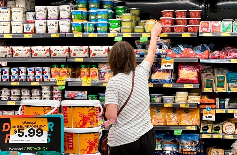 A woman reaches up for a container at a grocery store fridge containing cheese, fruit and yogurt.