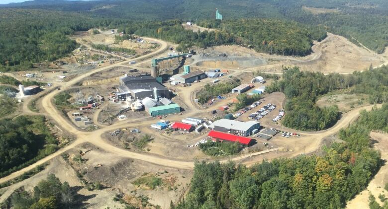 An aerial view of a mine site with various buildings and equipment surrounded by trees.