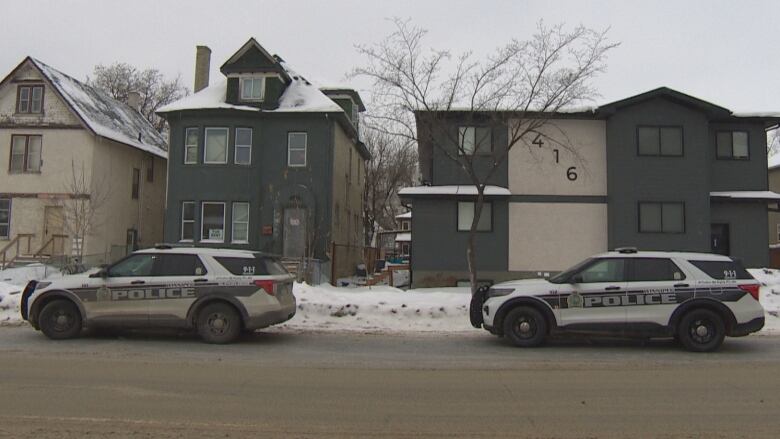 Two police vehicles parked on a street in front of several houses.