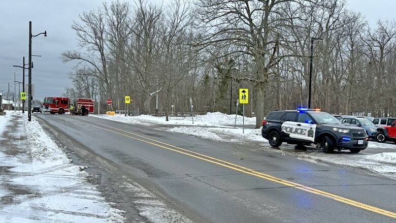 There is a road with a fire truck blocking it, and a police car with the lights on parked to the side.