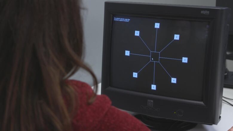 A woman sits in front of a computer screen with several squares on it. 