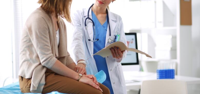 A doctor checks the pulse of a female patient as she sits on an examination table.