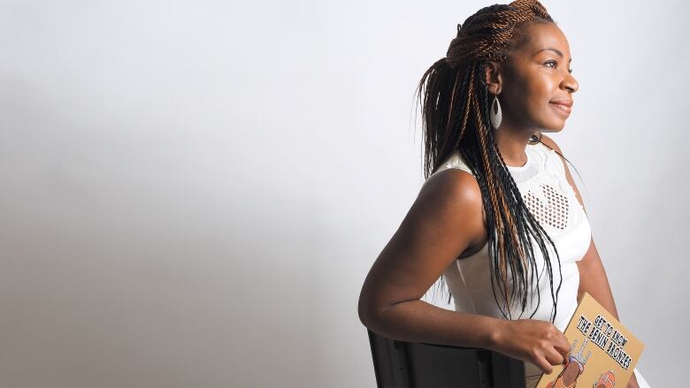 A Black woman with long braids holds a children's colouring book.