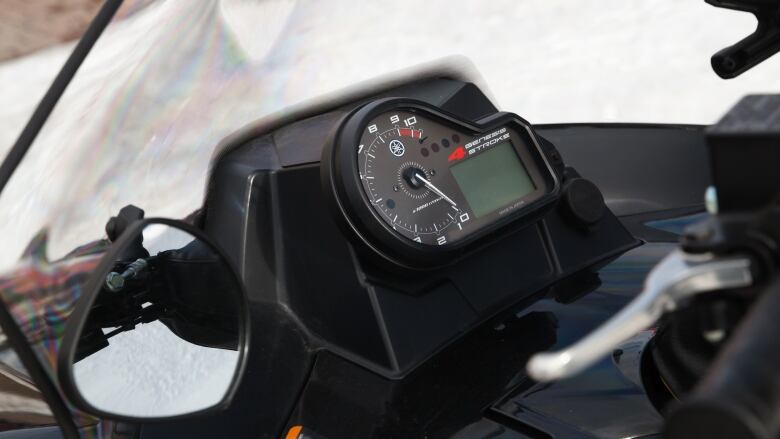 A closeup shows the speedometer and windshield of a snowmobile against a blurred white background.