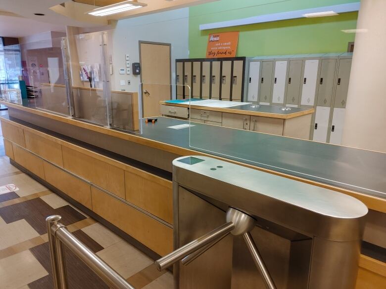 A turnstile stands in front of a long security desk protected by plexiglass. Behind the desk, lined against the wall, are storage lockers.