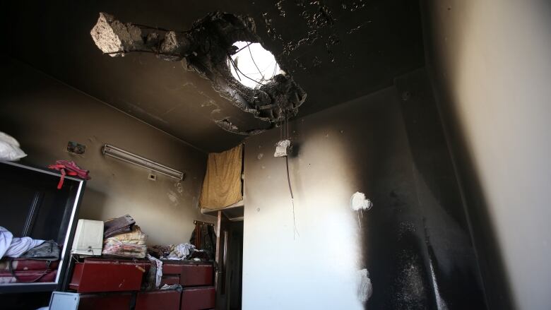 An apartment is shown with debris and rubble, a blackened wall and a hole in its ceiling.