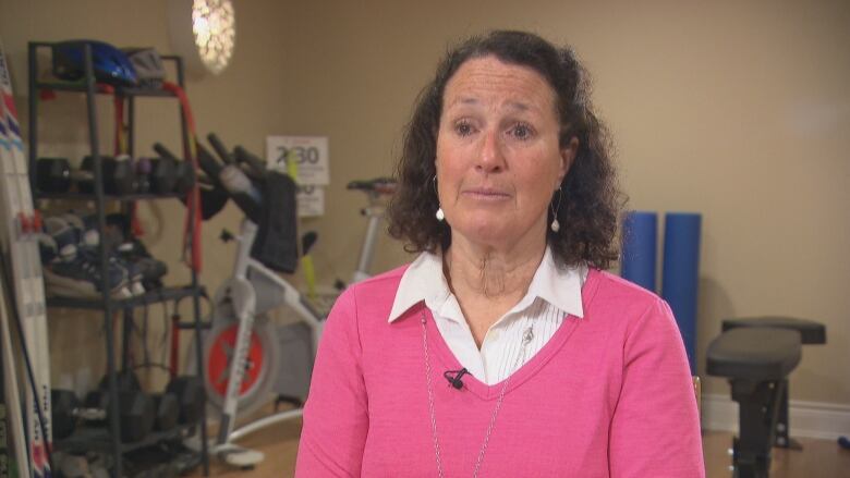 A woman in a pink sweater sits for an interview in front of assorted sports equipment.