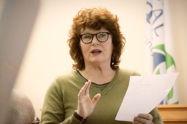 A woman holds a piece of paper and speaks.