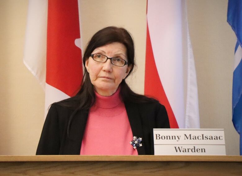 A woman sits at a desk next to a nameplate that says 