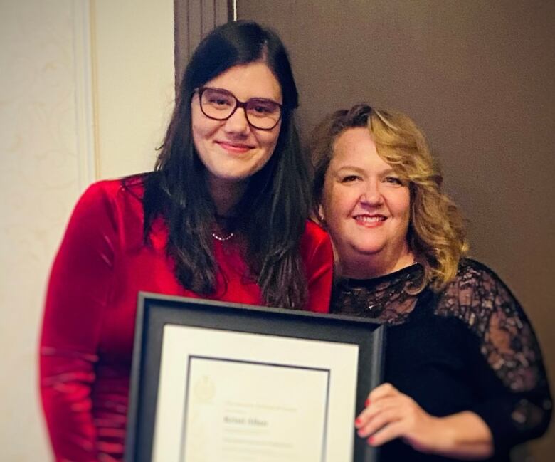 Two women pose with a framed certificate 