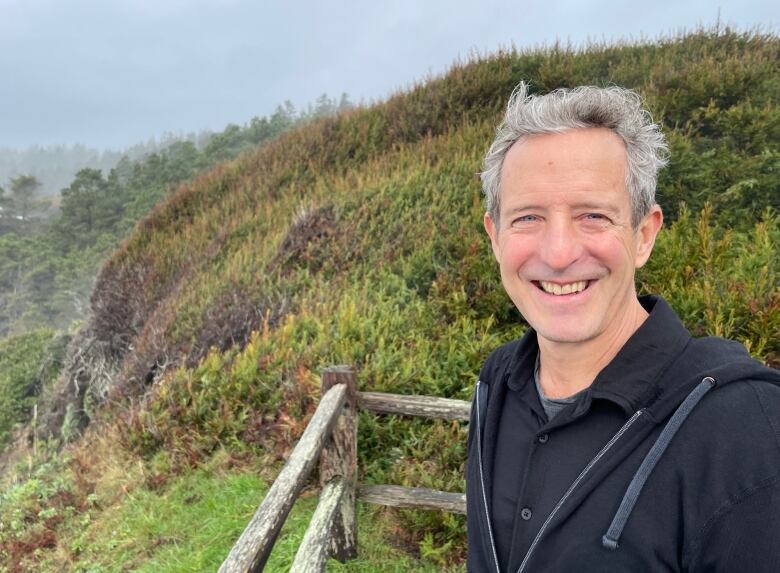 Edward Slingerland outside, with fence and shrub-covered hill in background