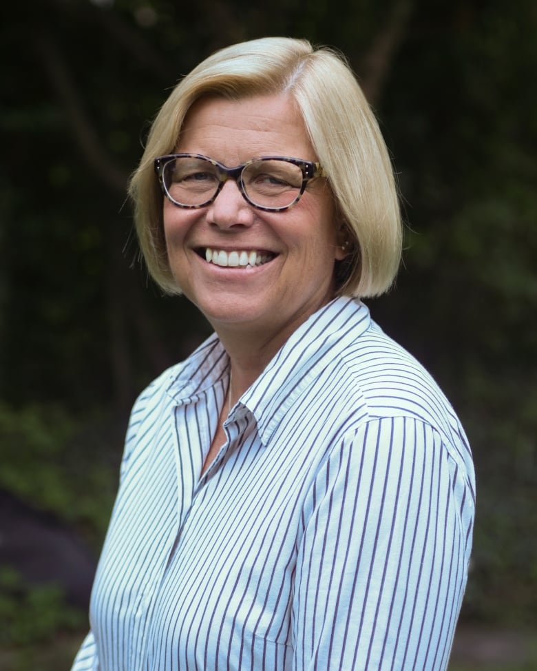 Smiling woman with short blonde hair wearing white and blue striped collared shirt. 