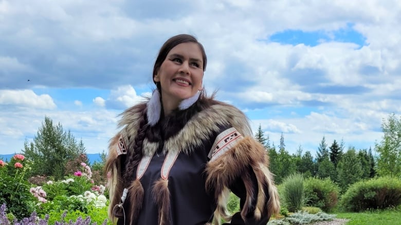 An Inuvialuit woman, dressed from head to toe in Indigenous-made items with fur, stands outside. 