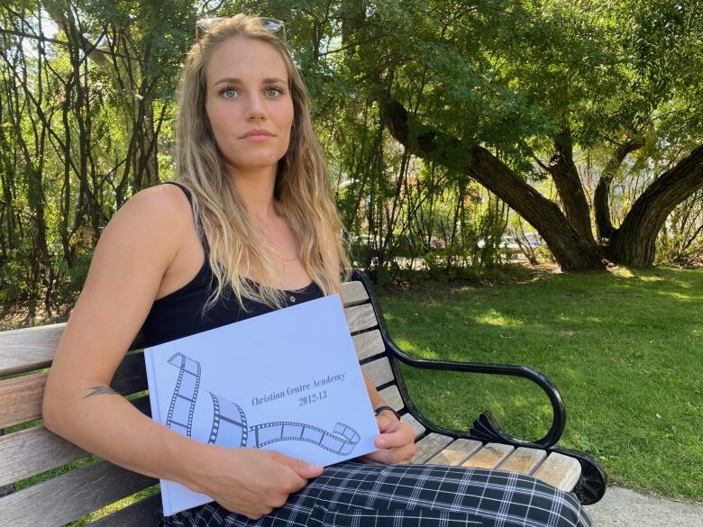 A woman sits on a bench outside. 