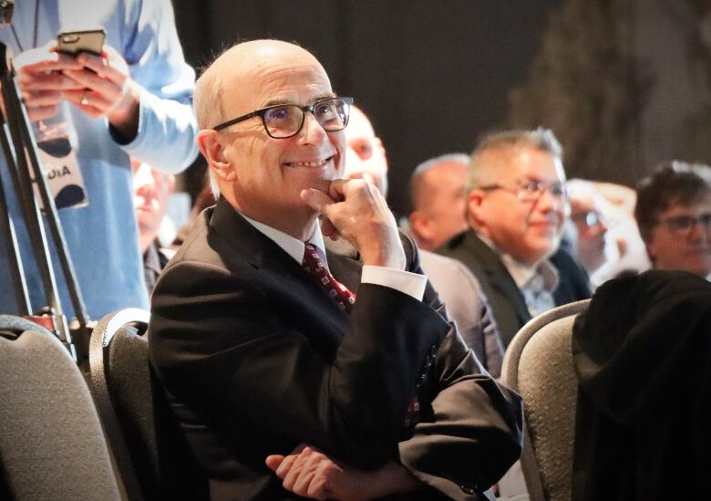 A man is seen sitting in a crowd, smiling.