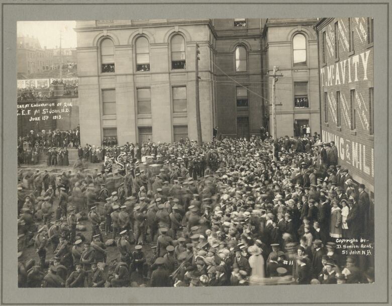 An old photo showing soldiers lined up on a city street, with a crowd of people cheering.