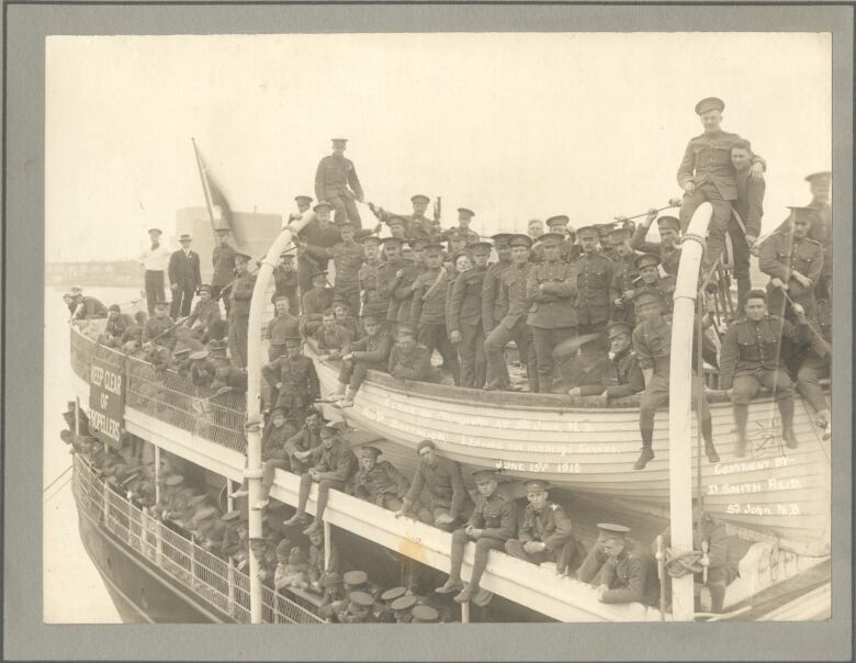 A ship with its deck crowded with soldiers sit's dockside.