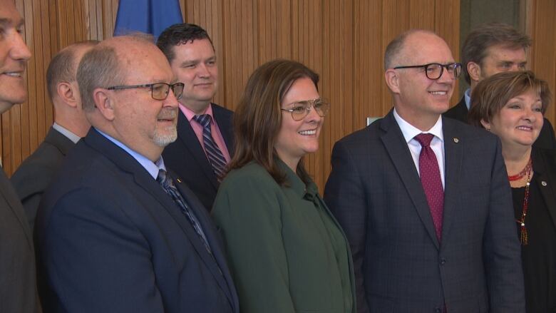 Premier smiling with other politicians outside a wood-panelled office at city hall.