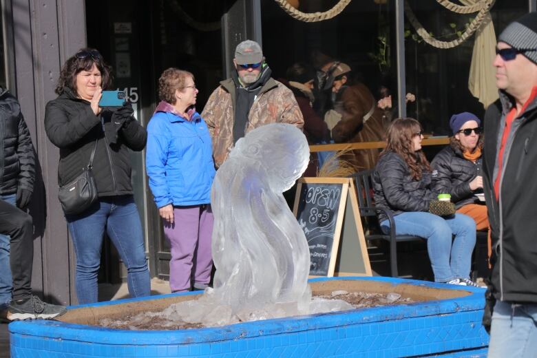 People stand in front of an ice sculpture of an octopus. 