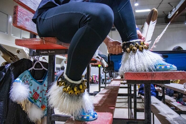 A man ties bells to his powwow regalia shoes.