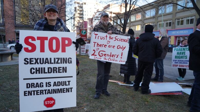 A man and a woman wearing hats and heavy coats hold signs that read, 