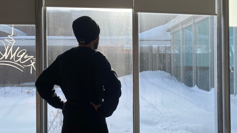 A man, staying in a warming shelter, looks out the window to a snow-covered area.