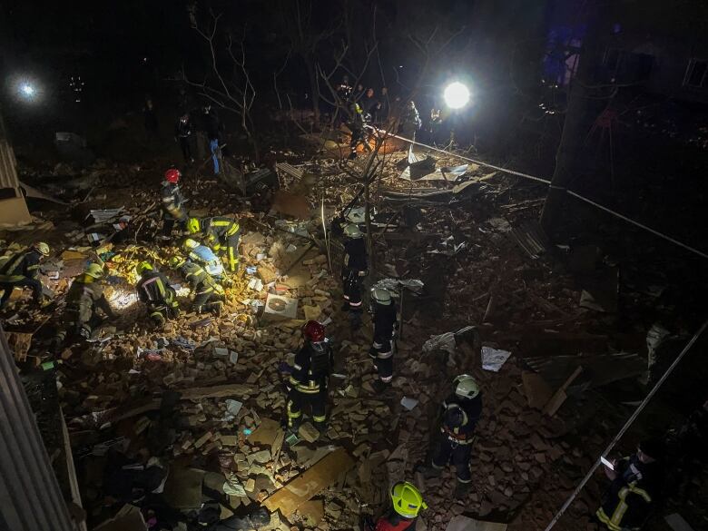 A bird's eye view shows firefighters digging through rubble.