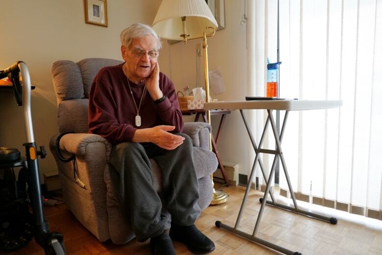 A portrait of an older man wearing glasses having a conversation in his apartment.