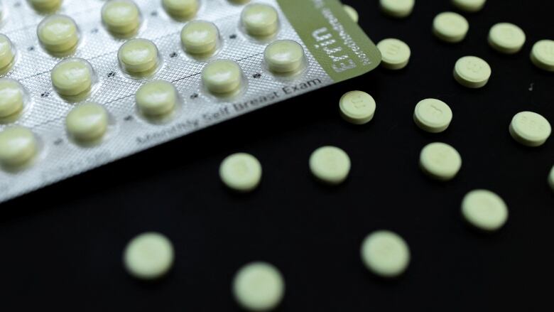 A foil tray of round pills with several individual pills spread out around it.